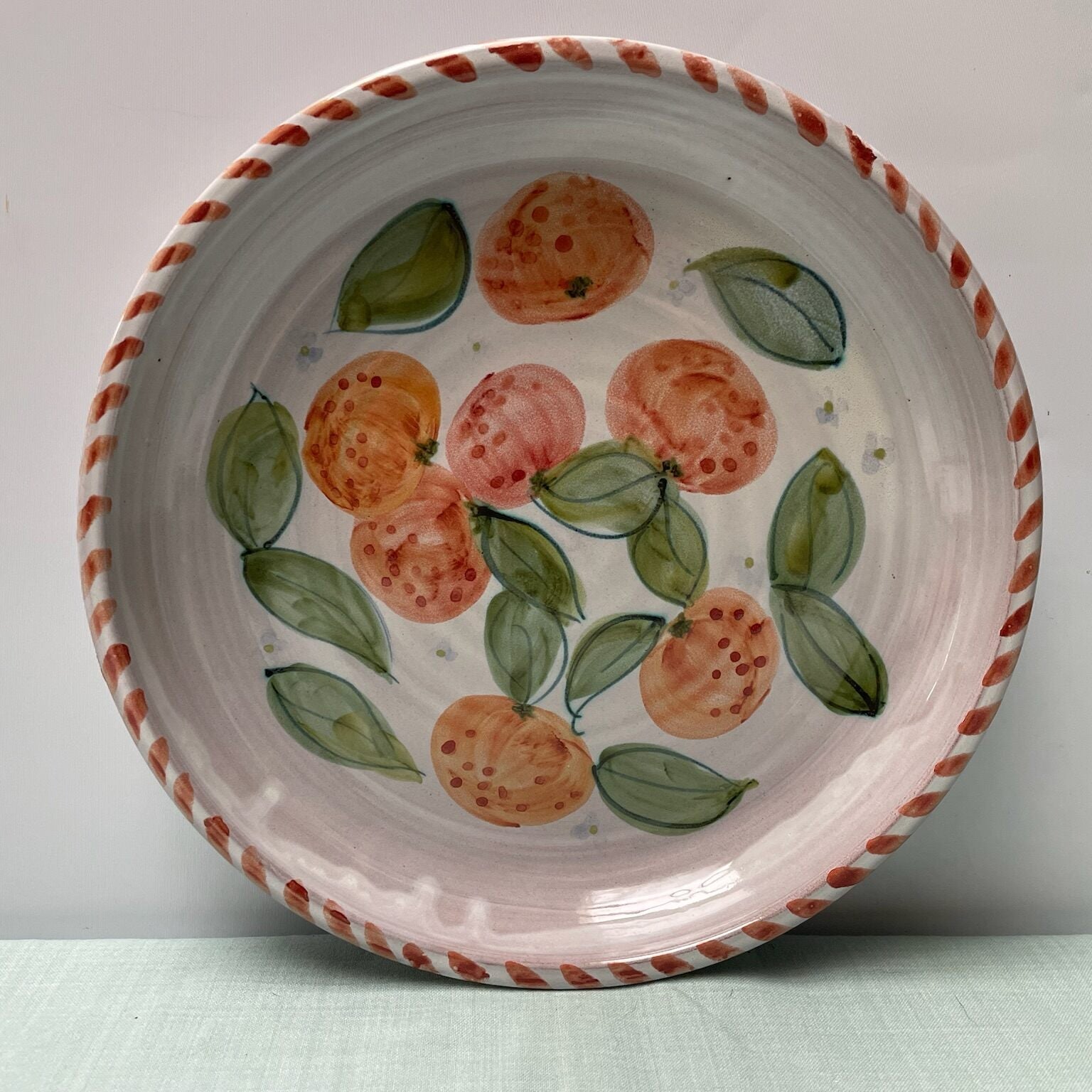 Ceramic bowl with hand-painted peaches and leaves on a plain background